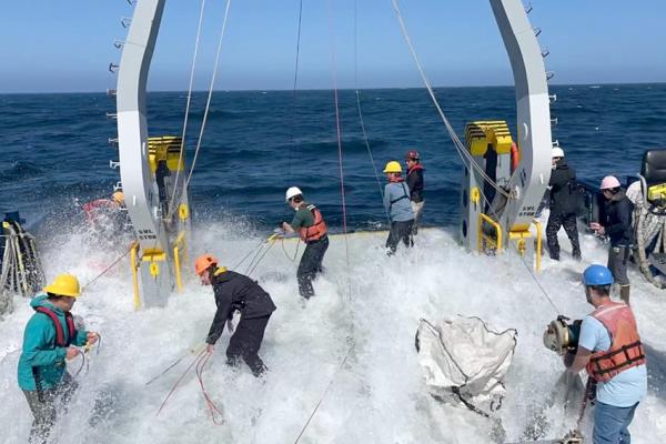 VIMS staff on a large vessel pull ropes as a big wave spills on deck