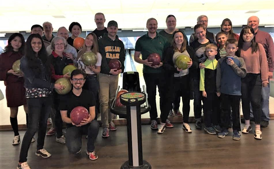 A group photo of International Family Network members at a bowling alley holding bowling balls