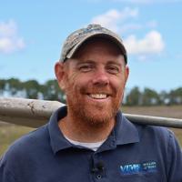 Matt Kirwan stands in a salt marsh posing with his sediment corer.